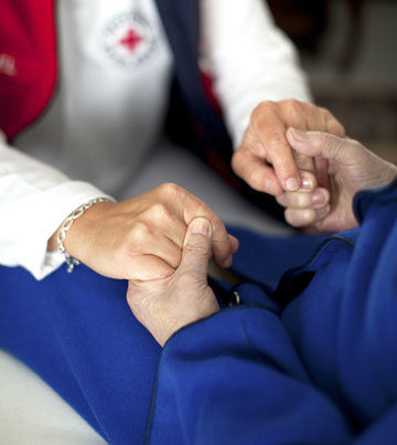 Pflegerin und Seniorin halten sich bei den Händen